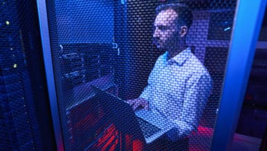 IT technician performing server administration while standing with laptop near server rack in data center