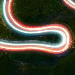 Visualizing 5G with electric light trails connecting destinations in mountain road at night in directly above view.